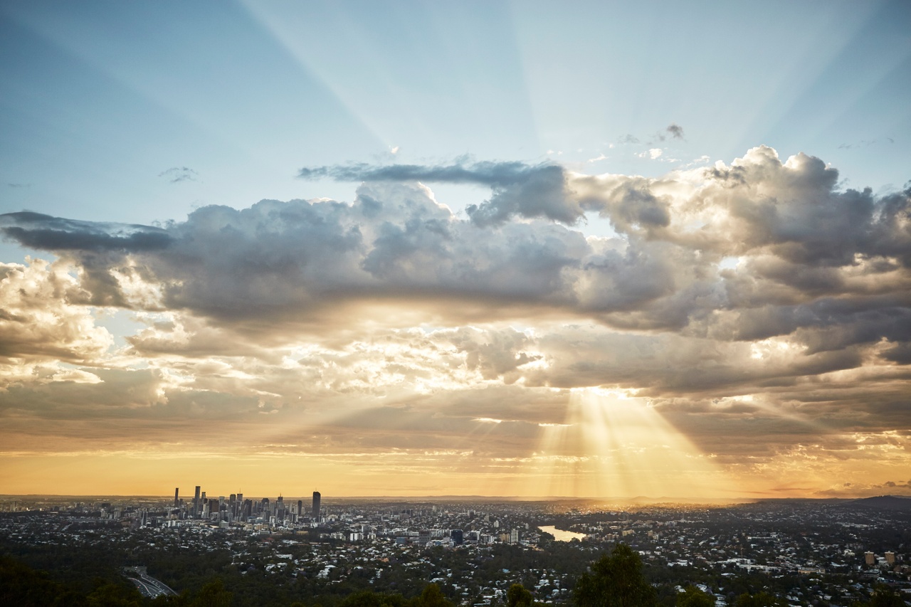 An image of golden sunlight radiating through clouds and cityscape at Mt Coot-Tha.
