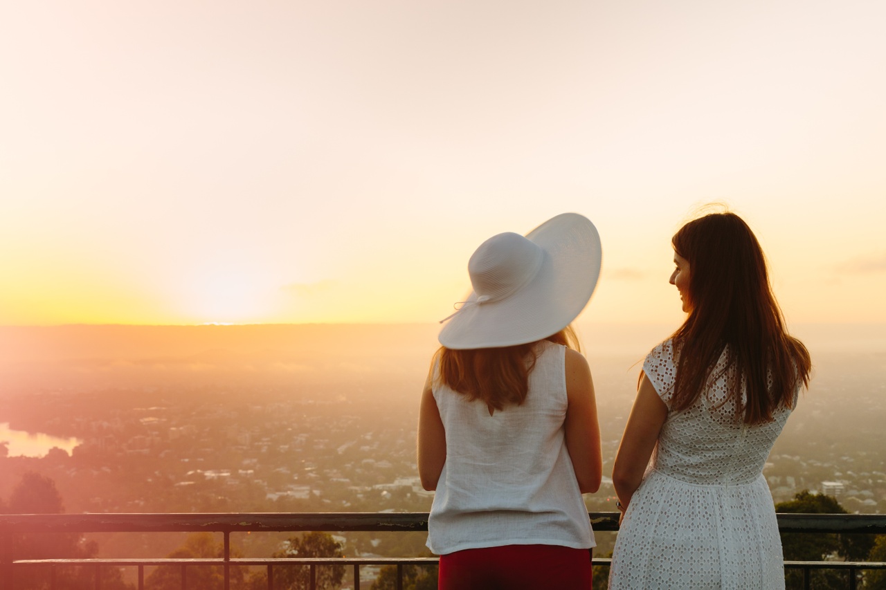 Two women in white looking at sunrise at Mt Coot-Tha Summit lookout.