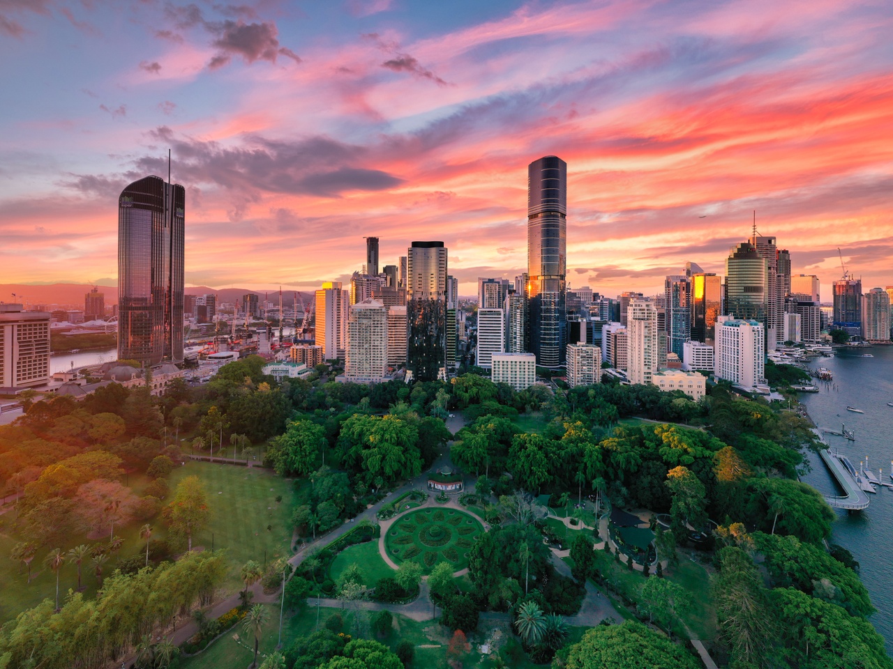 A bright pink sky frames the city skyline and rich greens of the Brisbane Botanic gardens.