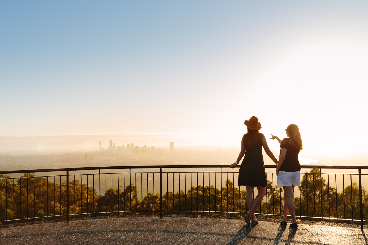 Two women looking at the cityscape from a lookout at sunrise at Mt Coot-Tha.