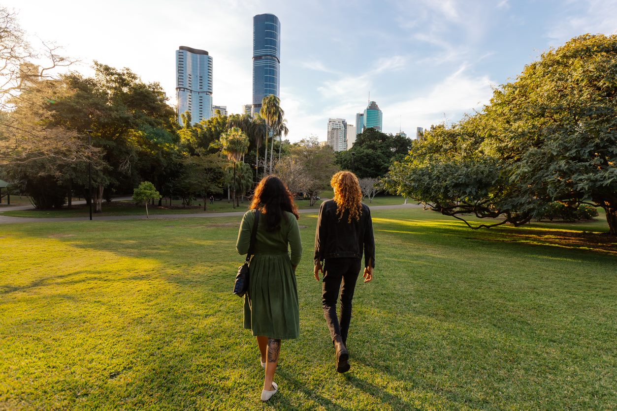 Two people walk through the City Botanic Gardens with city skyline in the background