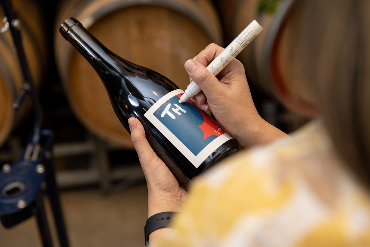 A woman is writing onto the label of a wine bottle in white pen at City Winery.
