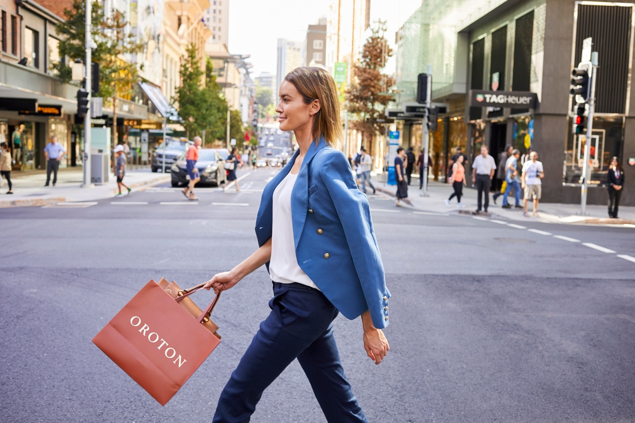  A profile image of a woman in blue jacket with shopping bags in hand crossing the road at the city. 