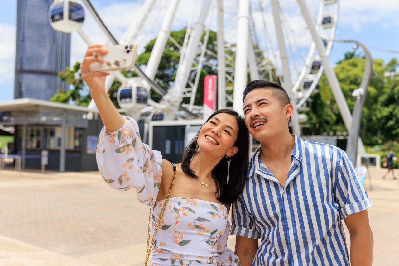 Close up shot of a couple taking a selfie in front of the Wheel of Brisbane.