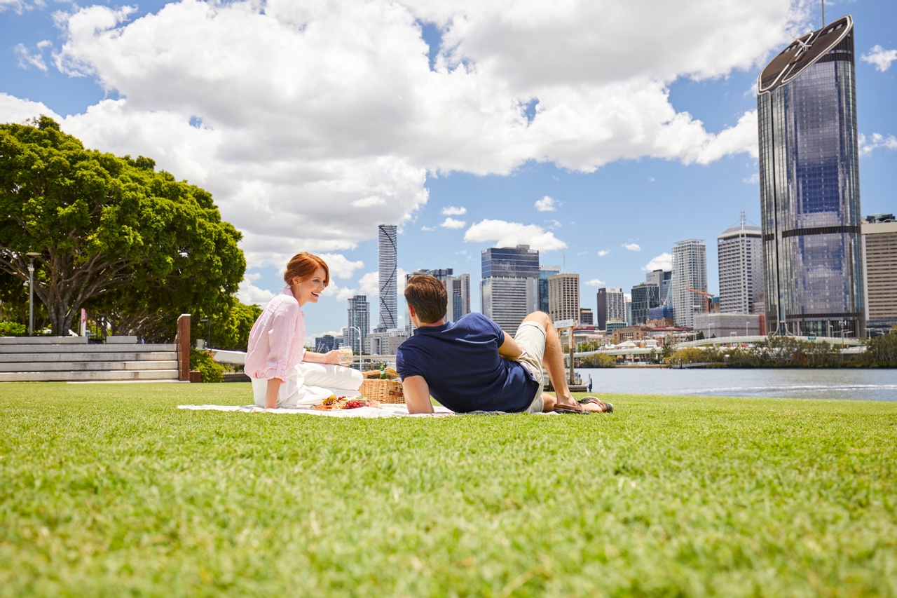 A man and a woman is picnicking on grass by the riverside at South Bank.