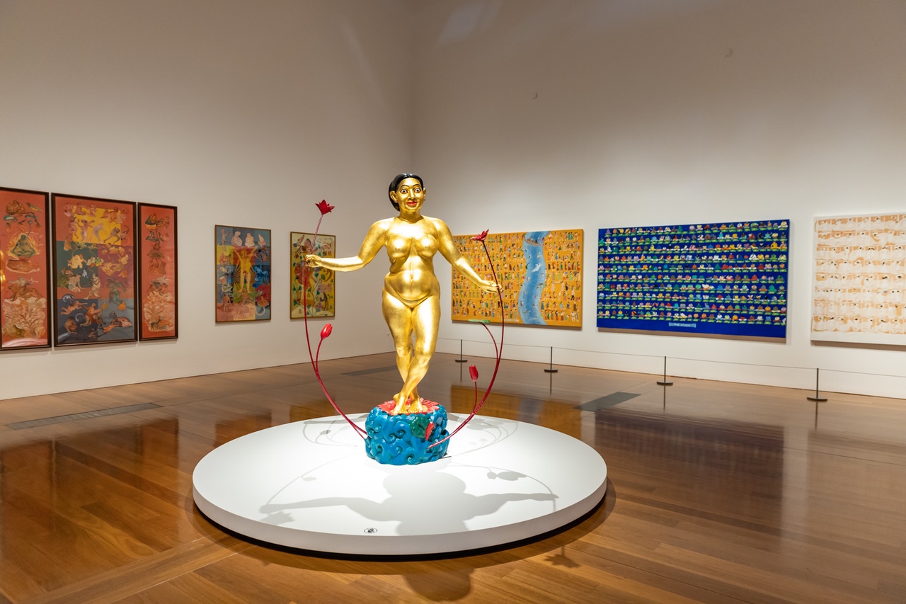 A golden sculpture in an art gallery, surrounded by paintings.