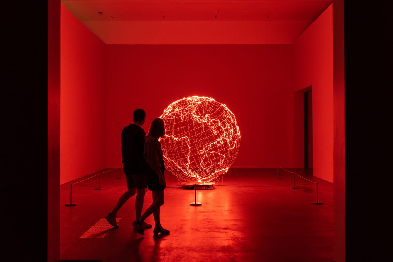 Two people visit a QAGOMA exhibition bathed in red light