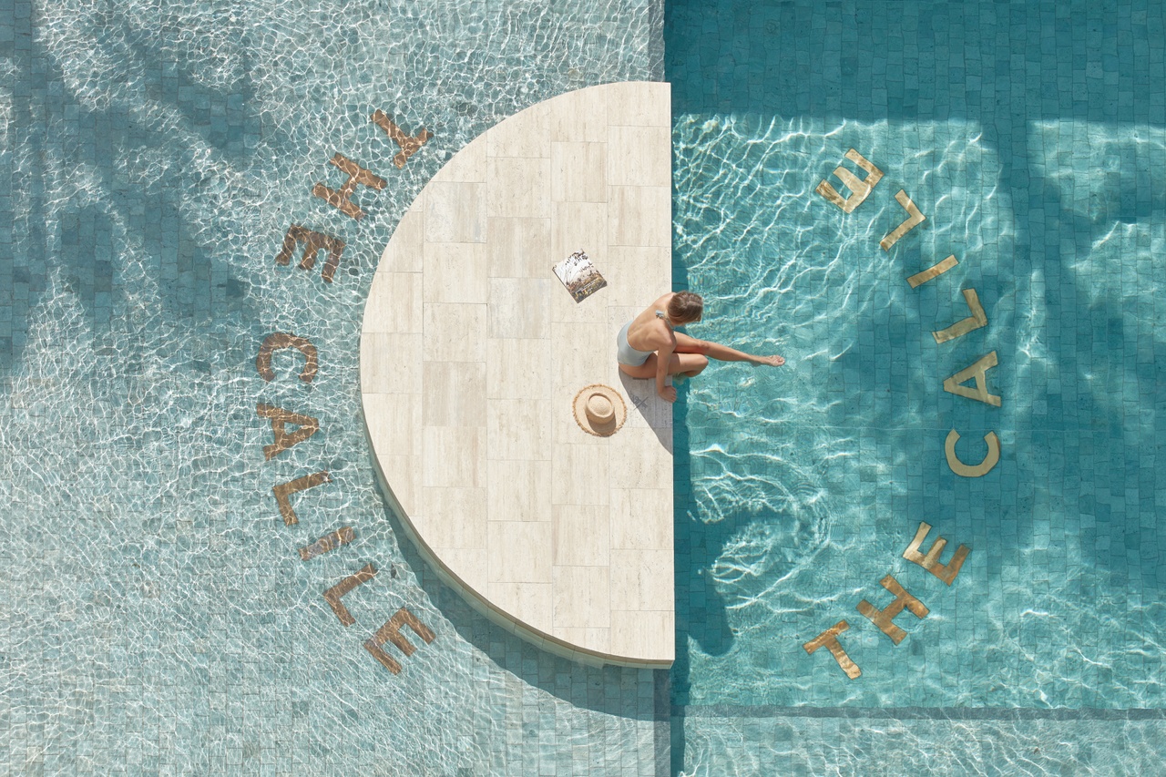 Overview of a women relaxing with her hat nearby on a platform on the pool at The Calile