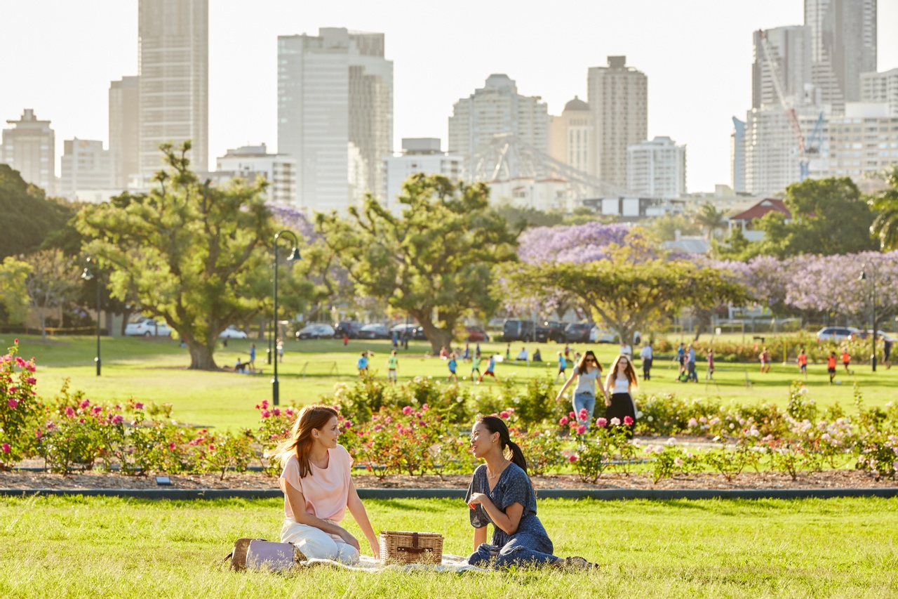 Two females having a picnic on the lawn at New Farm park with cityscape as background at New Farm.