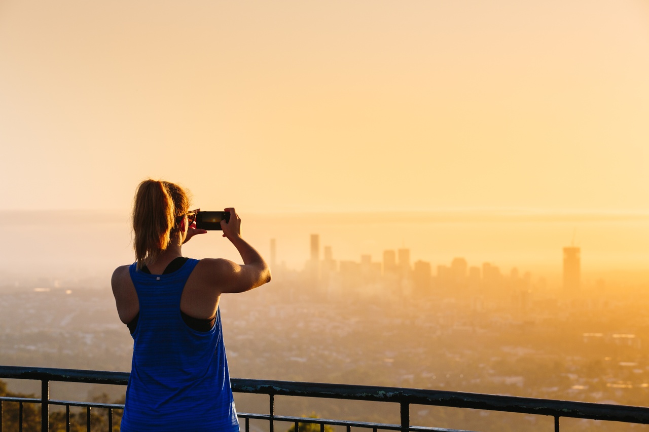 A woman taking a photo of orange colour theme city view at sunrise on a lookout_Mt Coot-tha