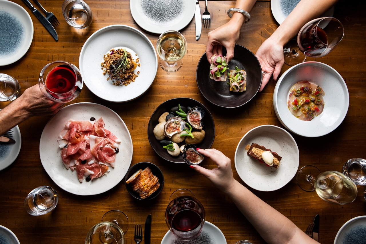 An image of some European dishes with hands holding the food and glass of wine.