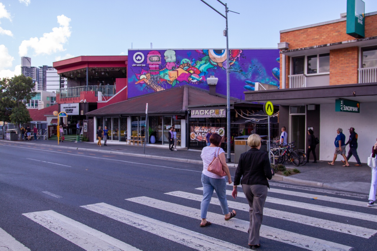 Two women crossing Boundary St and a purple colour theme mural on one of the buildings