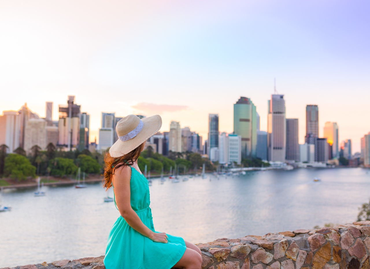Female sitting on the walkway edge at Kangaroo Point cliffs overlooking the Brisbane River with a colourful sunset.