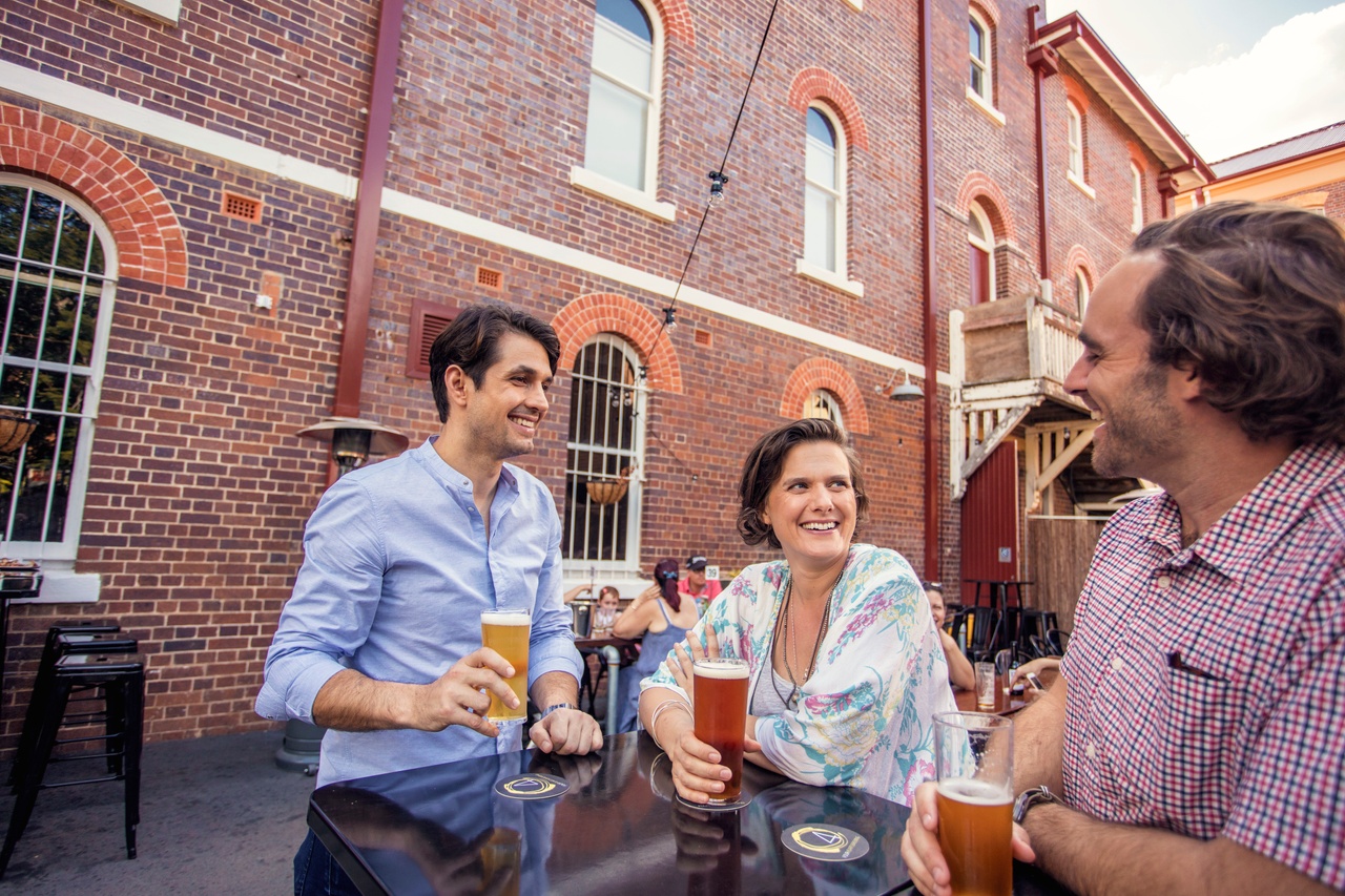 A group of friends drinking beer in a outdoor area of a brick building at Ipswich.