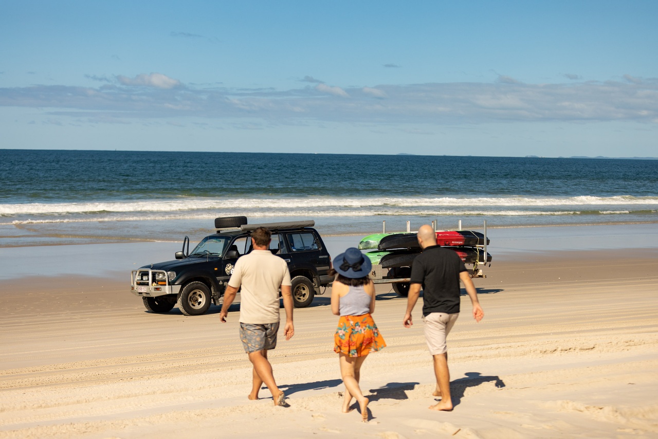 Three people walking towards a 4WD on the beach at Bribie Island.
