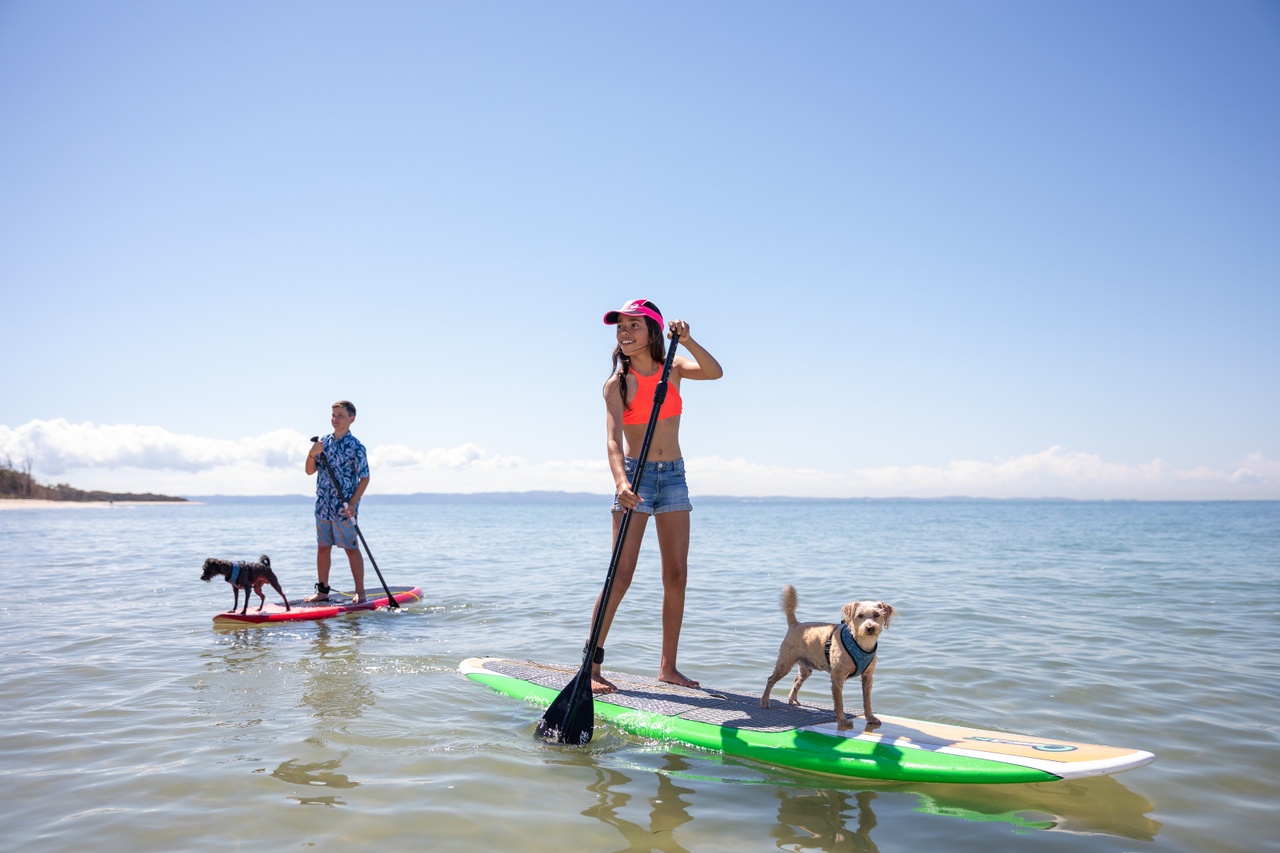 A teenager and a young woman Stand Up Paddling with their dogs at Red Beach.