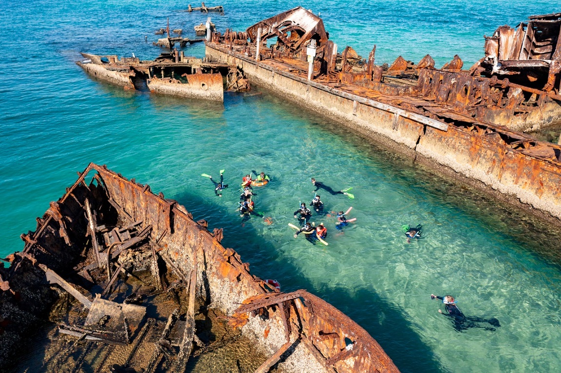 An aerial drone shot of the Moreton Bay shipwreck and surrounding water with people snorkelling the Tangalooma Wrecks