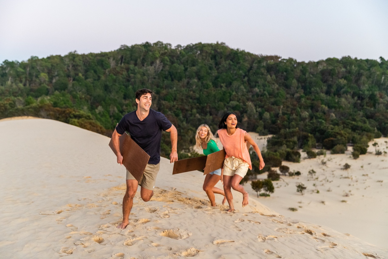 An image of a group of three friends running up a hill with boards on Moreton Island.