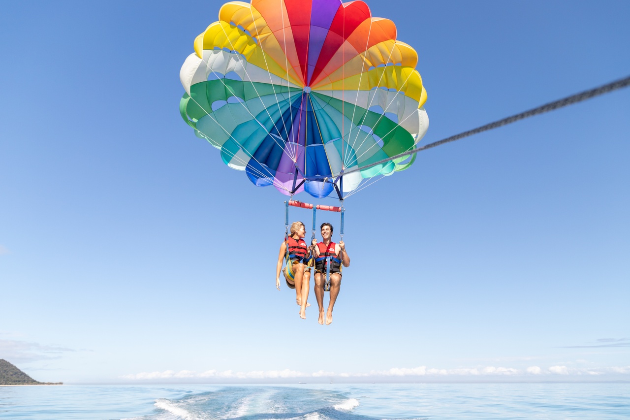 A couple parasailing over the water with a rainbow parachute