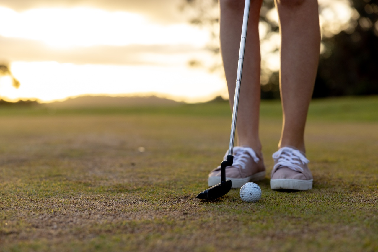 A close up of a woman hitting a golf ball with a golf club.