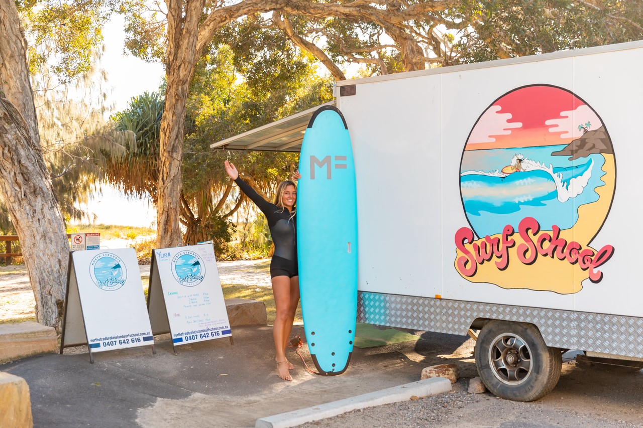 A surfer taking the picture with a surfing board next to a van on North Stradbroke Island.