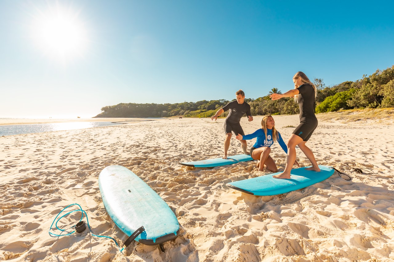 Two people learning to surf with a coach at North Stradbroke Island/Minjerribah