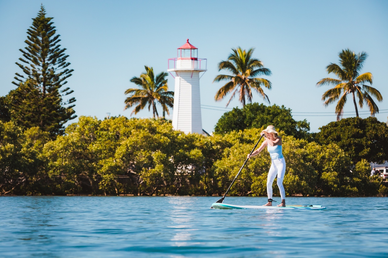A woman stand up paddling on the water next to Cleveland Point Lighthouse.