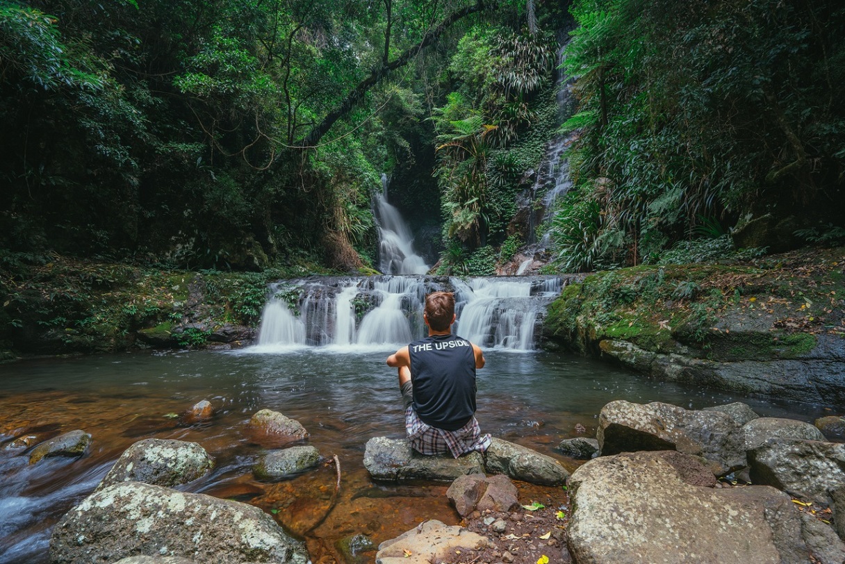 A man sitting on a rock in front of a waterfall at Scenic Rim.