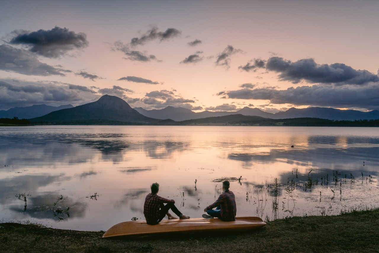 Two people sitting on a kayak upside down by a lake at sunset, Lake Moogerah, Scenic Rim