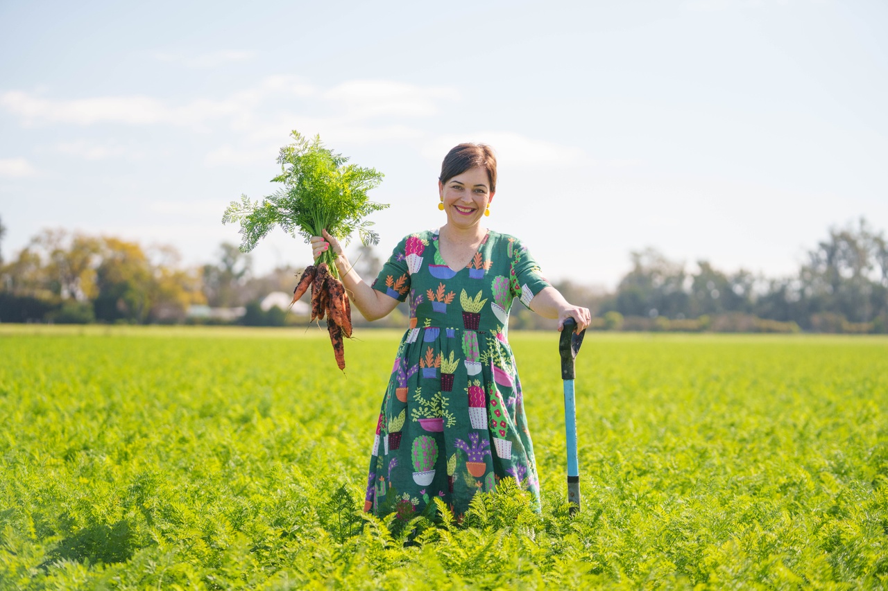 A woman standing in a field holding a bunch of carrots at Scenic Rim Farm Box.